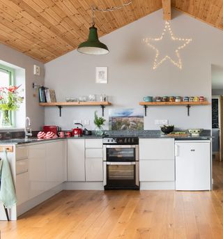 kitchen with white units with black granite worktops and wooden ceiling and floor and green pendant light and star fairy lights
