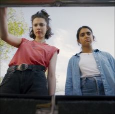seen from the pov of a car trunk, a woman (margaret qualley) lifts the trunk's hood while another (geraldine Viswanathan) stands next to her