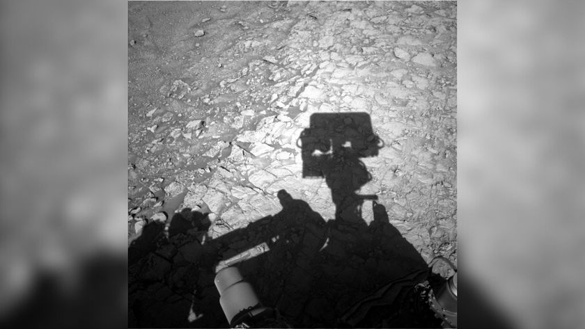 A gray-scale photo showing a shadow of NASA&#039;s Curiosity Mars rover on the ground, with its square Mastcam &quot;head&quot; overlaid on a rocky terrain of &quot;boxwork&quot; patterns across the Martian landscape.