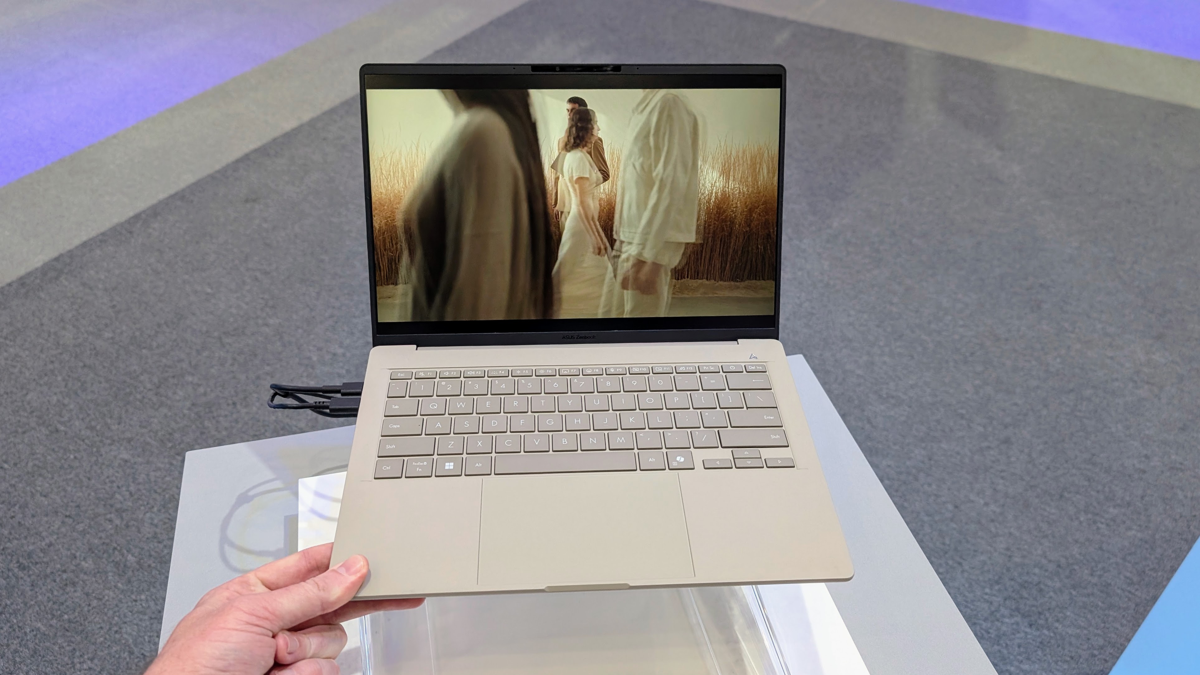 The Asus Zenbook A14 held with fingers and thumb to show how lightweight it is