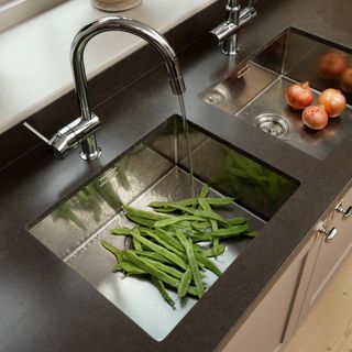 Freshly harvested onions and runner beans rinsed under water in kitchen sink