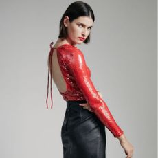 Brunette woman wearing red sequin top and black leather skirt with grey background