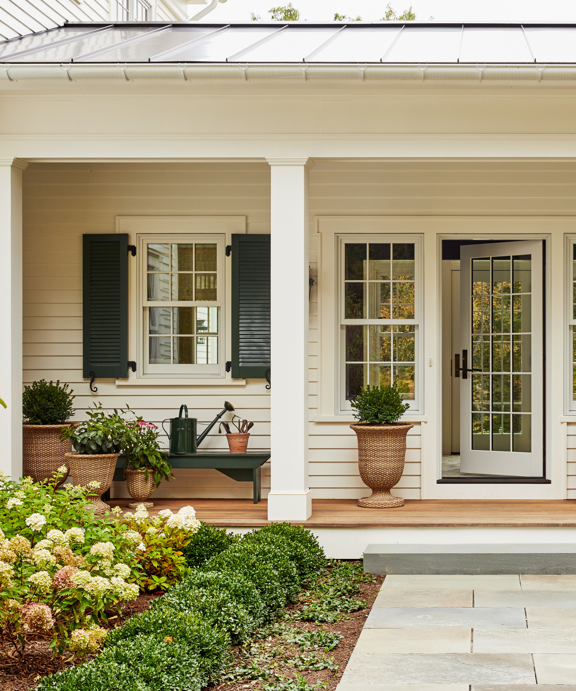 the exterior of a home with a large porch decorated with lots of plants and some plants in rattan planters