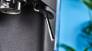 a black espresso machine by kitchenaid photographed against a blue background with silver chrome buttons and a pressure dial and steam wand