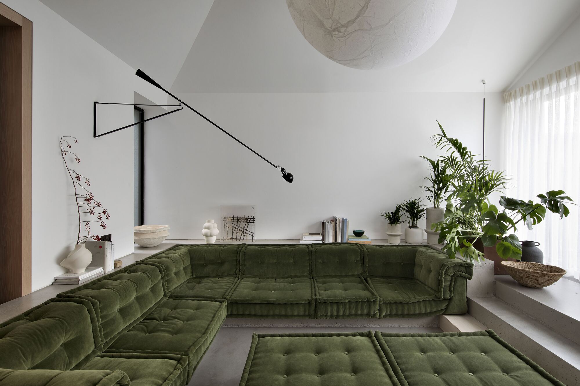 sunken conversation room in modern home with concrete floor and steps, sloped ceiling, swing arm light, vases and plants styled around the room