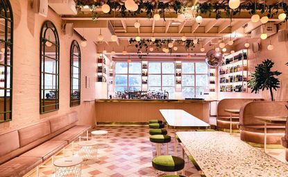 Pink colour bar, tables topped with terrazzo, pink and cream floor tiles that are laid in an asymmetrical pattern, and pendant globes, which hang from the ceiling in a representation of peaches on a tree.