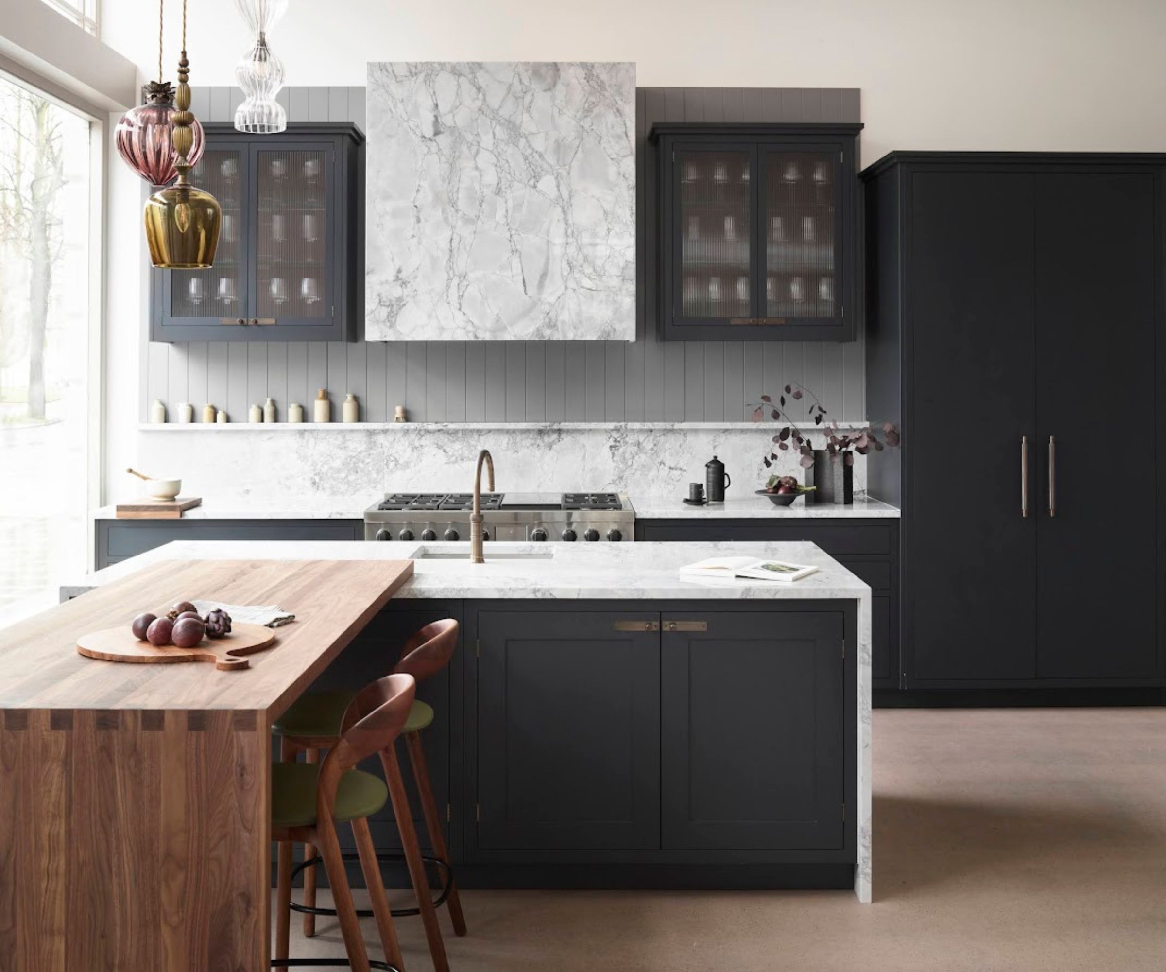 A contemporary kitchen with dark blue cabinets, a marble countersplash, and a marble waterfall island with a wooden counter to the seating area