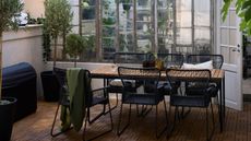 IKEA extendable table on an outdoor balcony with greenery, black dining chairs, string lights, and potted plants