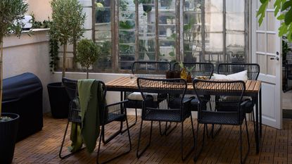 IKEA extendable table on an outdoor balcony with greenery, black dining chairs, string lights, and potted plants