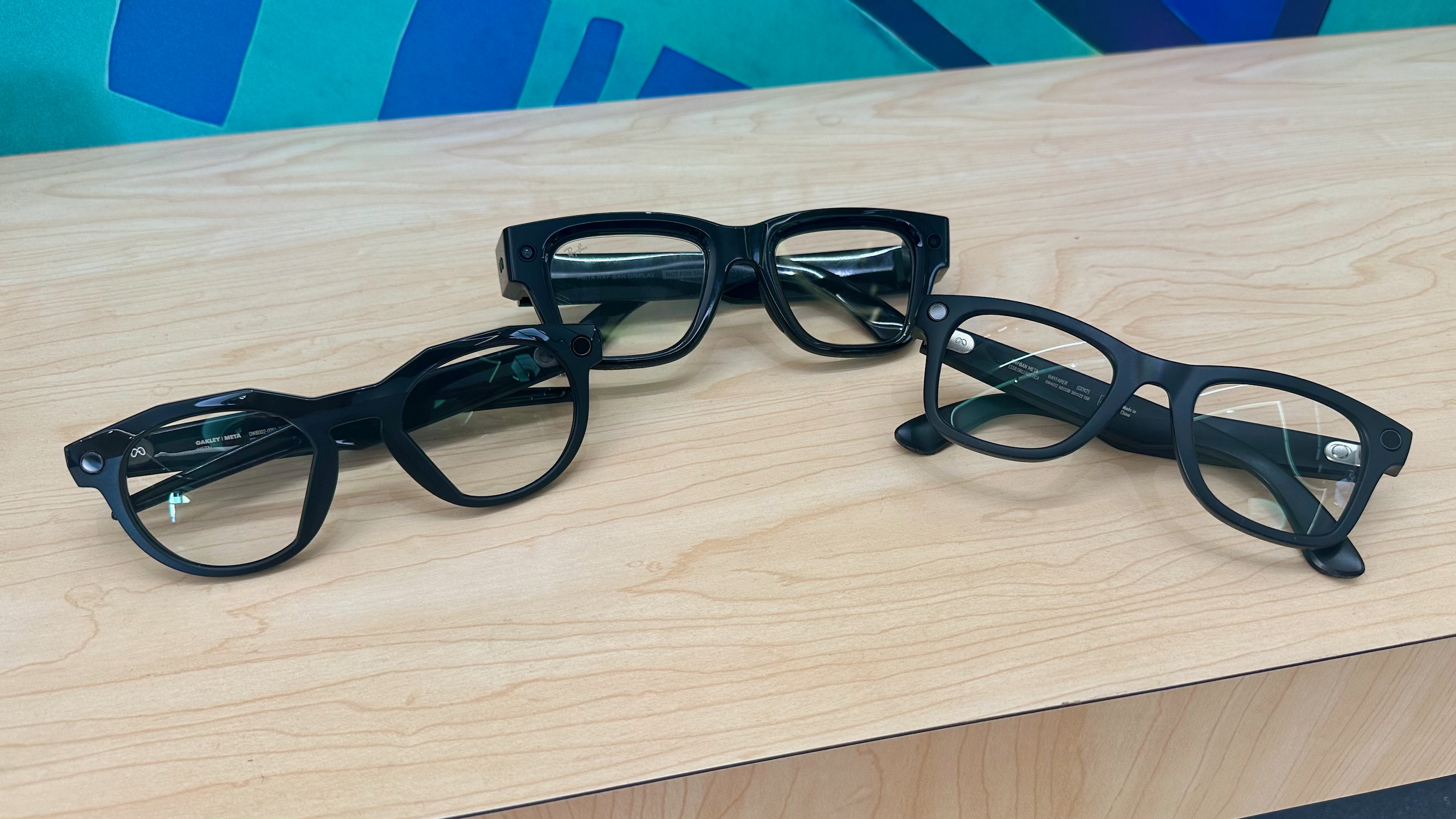 A photo of Oakley Meta HSTN (left), Meta Ray-Ban Display (center), and Ray-Ban Meta Gen 2 (right) smart glasses sitting folded next to each other, showcasing their different designs.