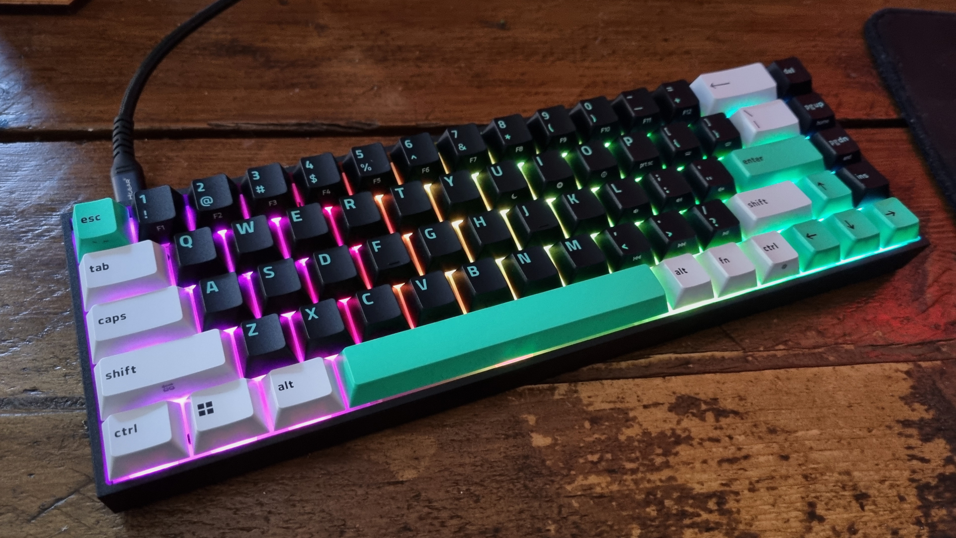 A Razer Reclusa X Mini 65% gaming keyboard with rainbow-coloured RGB lighting on a wooden desk