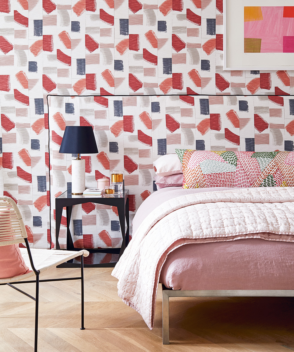 Bright, abstract wallpaper ideas for bedrooms illustrated in blue, pink and gray with matching headboard and a pink and white dressed bed.