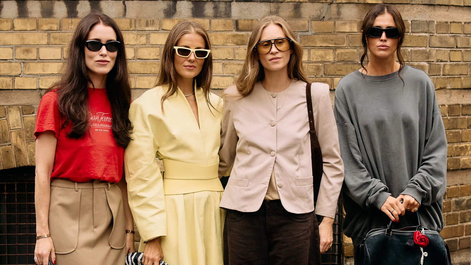 One woman wears red shirt and khaki pants, One model wears a yellow dress. The next woman wears a blazer and black pants, and the last one wears a gray sweater and skirt. 