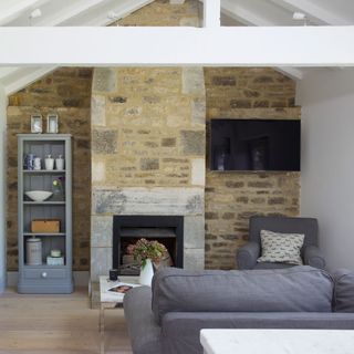 brick wall living room with a fire place and a wall-mounted tv , accessorized with a grey sofa and chair with a coffee table