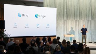 Yusuf Mehdi, Microsoft Corporate VP of modern life, search, and devices, speaking on stage next to a large screen displaying the Bing and Edge logos 