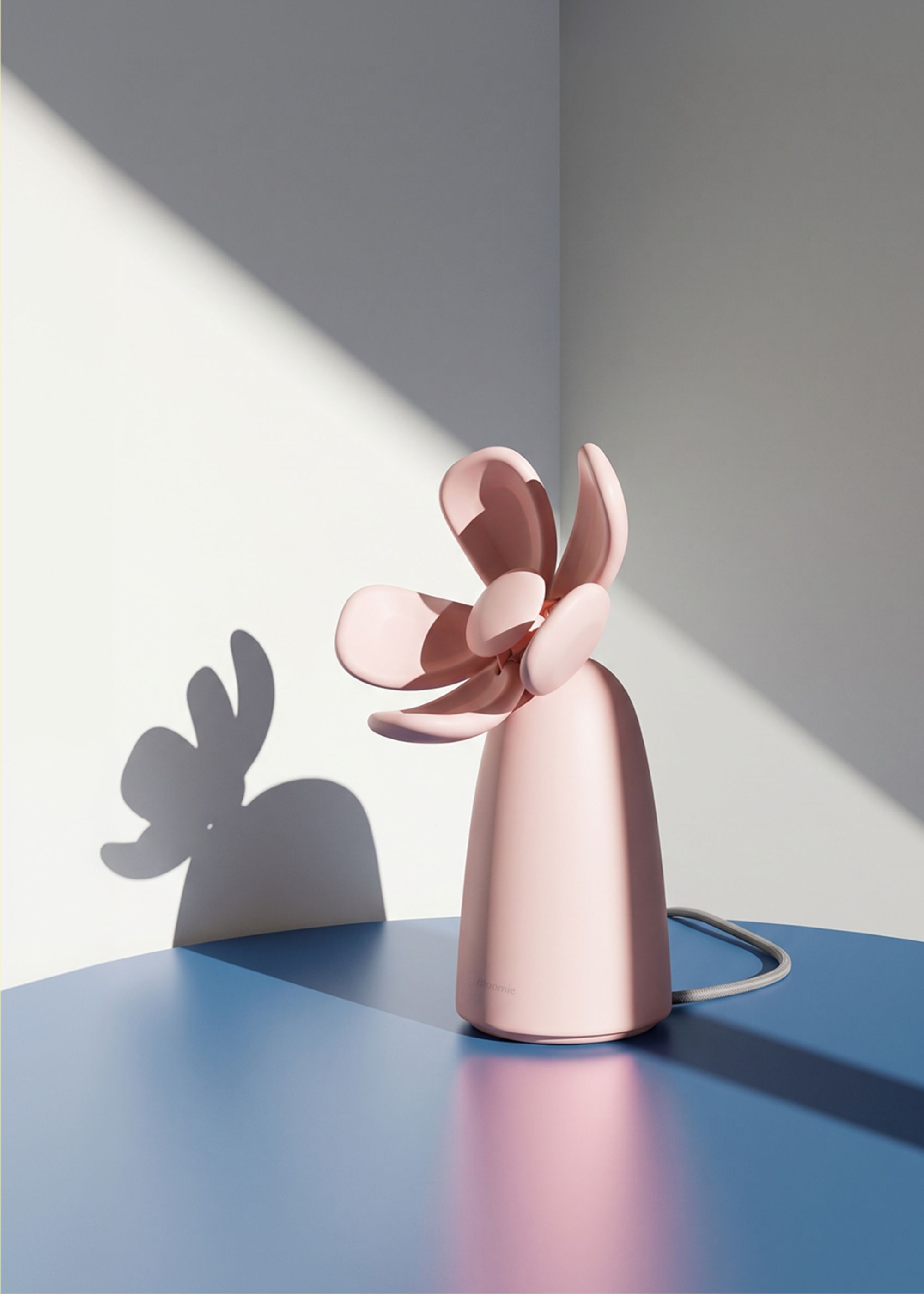 A blush pink flower-shaped air quality checker from Bloomie on a blue table in a white room