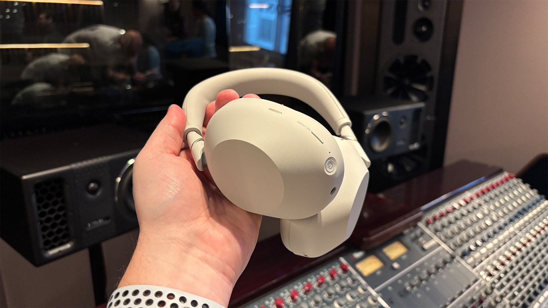 Sony WH-1000XM6 over-ear headphones held in hand in studio in front of mixing desk