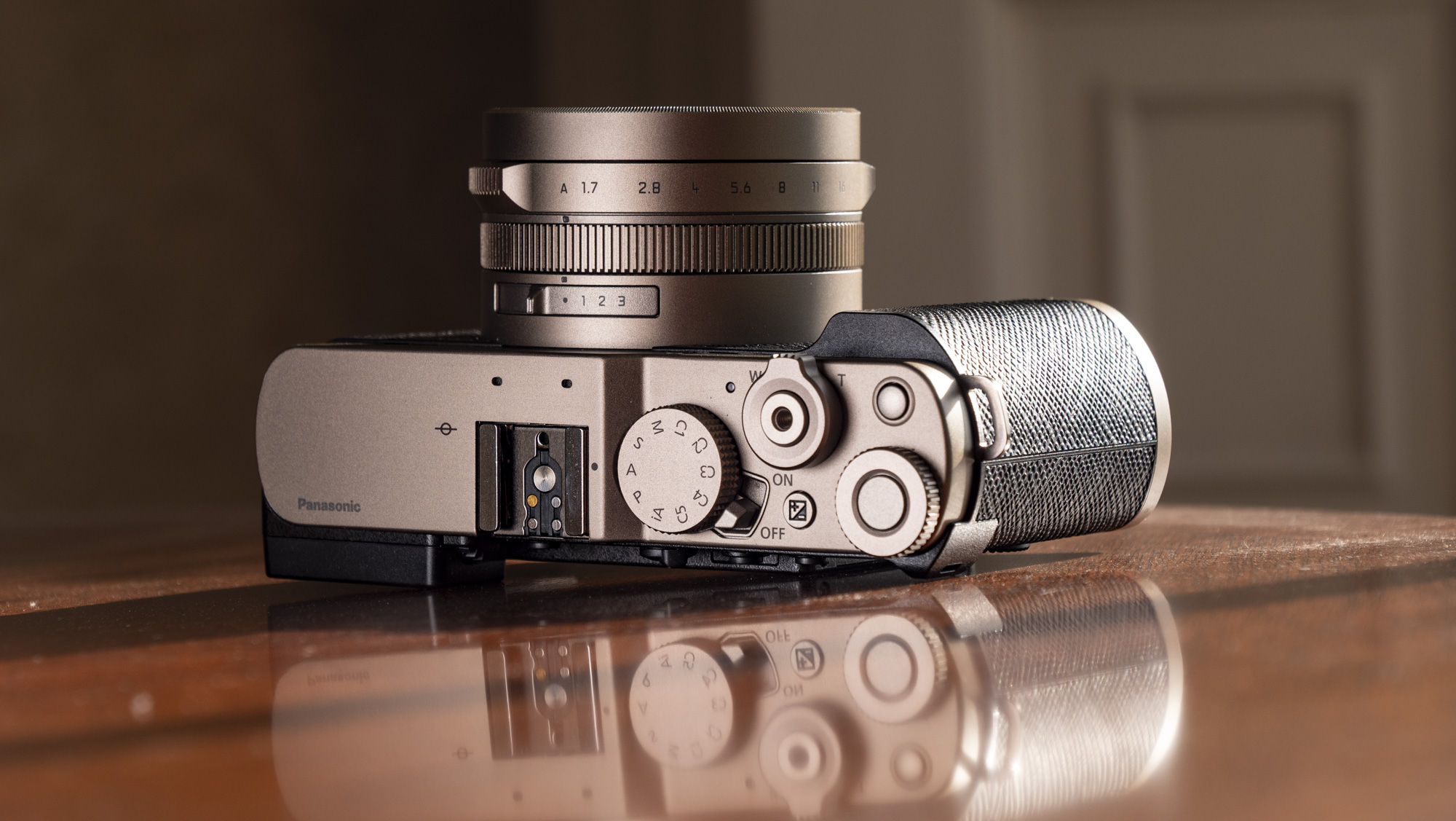 Titanium Gold special edition of the Panasonic Lumix L10 compact camera, laid on its back on an antique wooden table