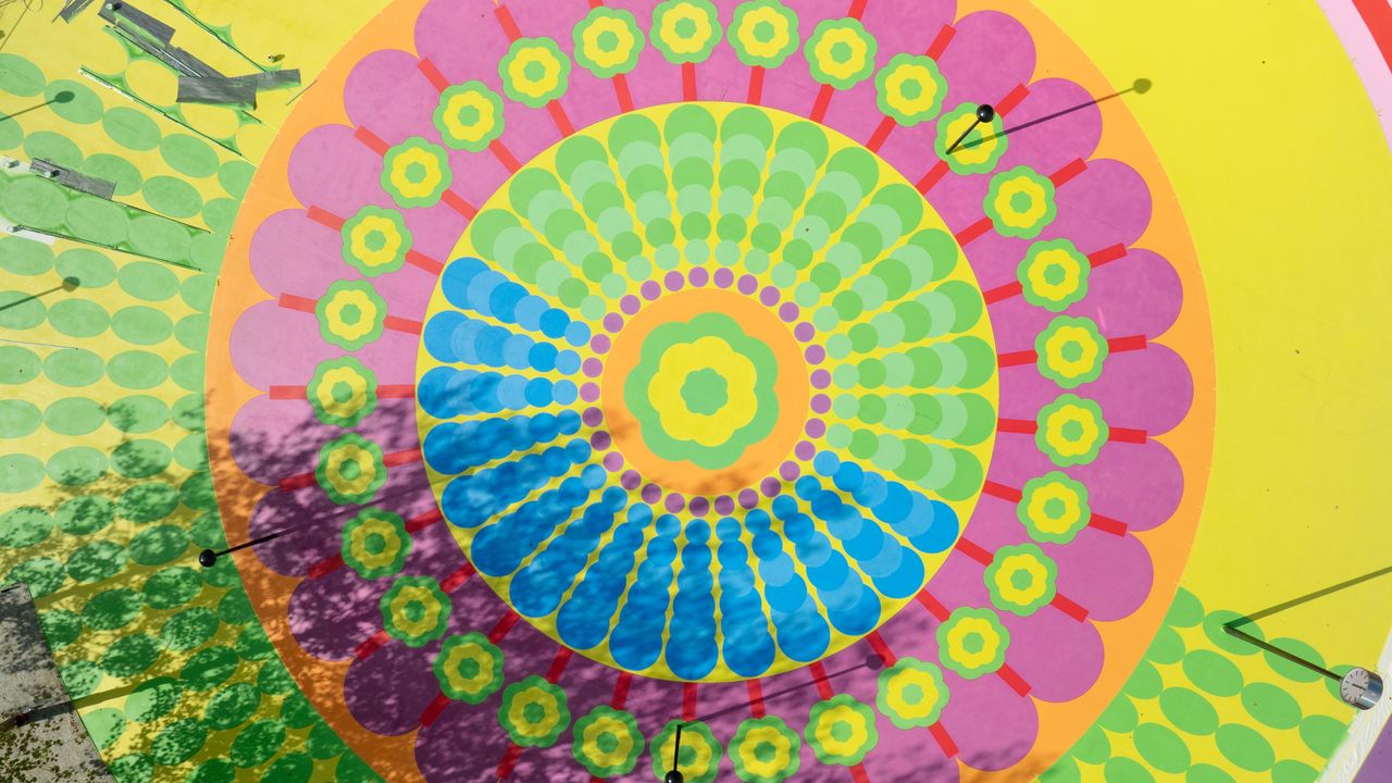 An aerial view of a colorful mural composed of concentric shapes in red, pink, orange, green, and yellow, including flowers, drops, and circles.