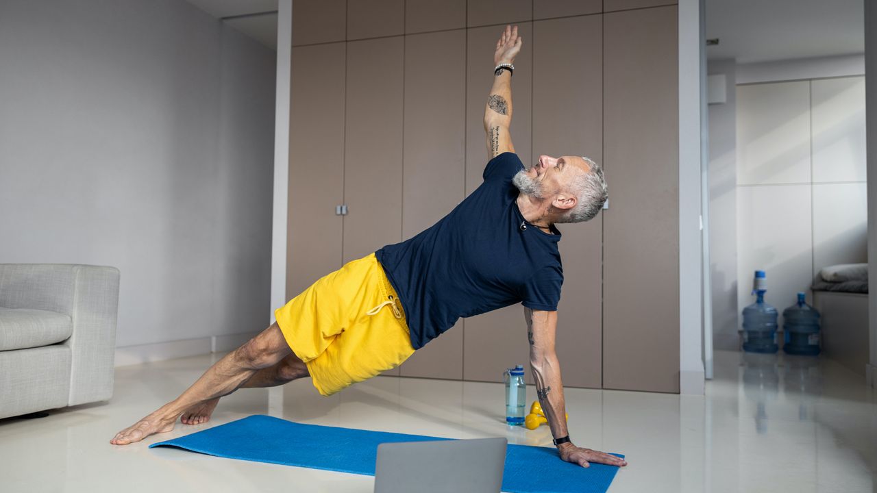 Muscular male easily holding his body above the floor while leaning on one hand and legs and lifting another arm