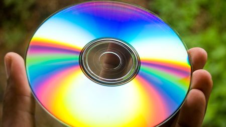 A Blu-ray disc held in a hand, so that its reflective surface catches the light 