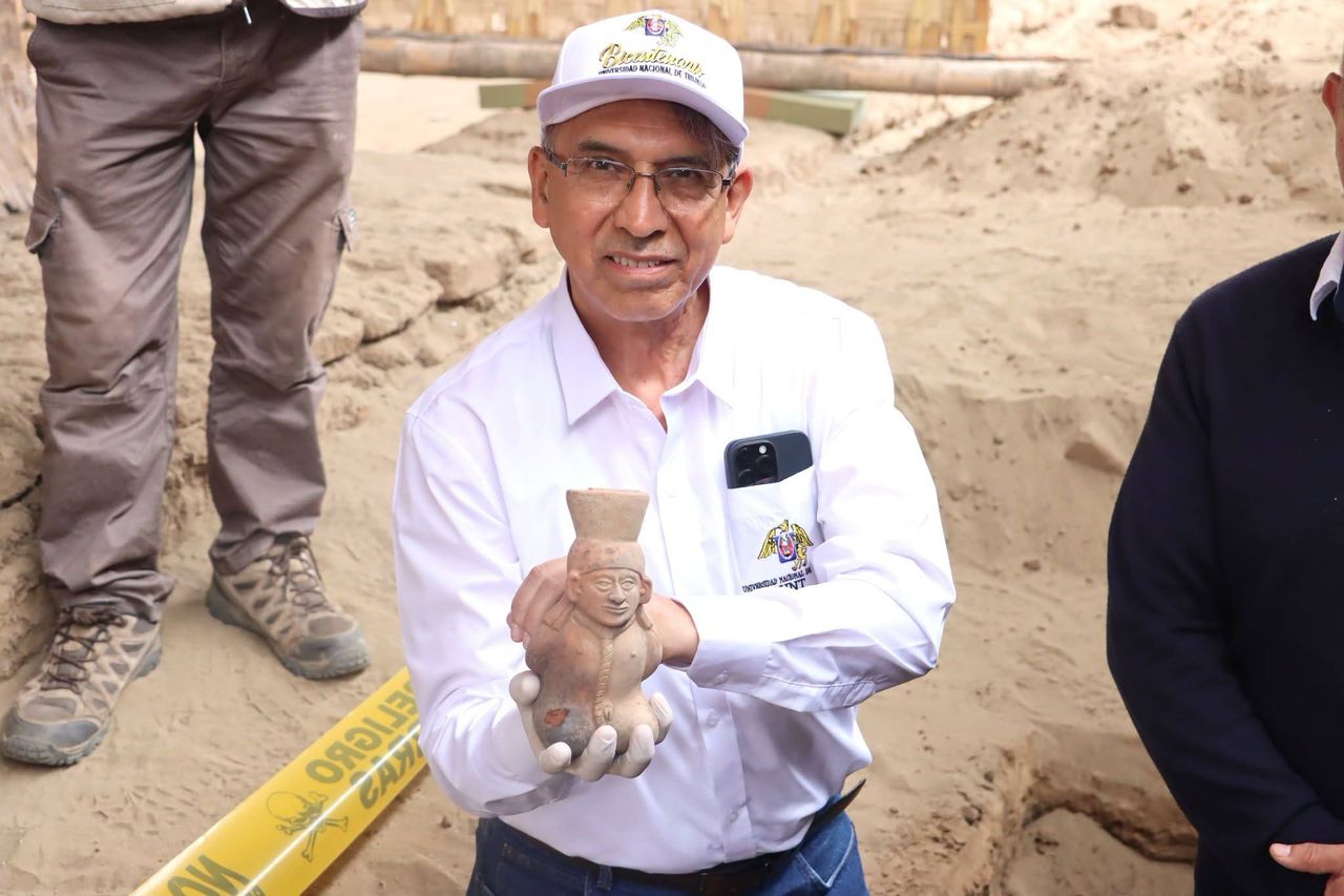 A man in a nice shirt and a baseball hat holds a piece of Moche pottery at an excavation site.