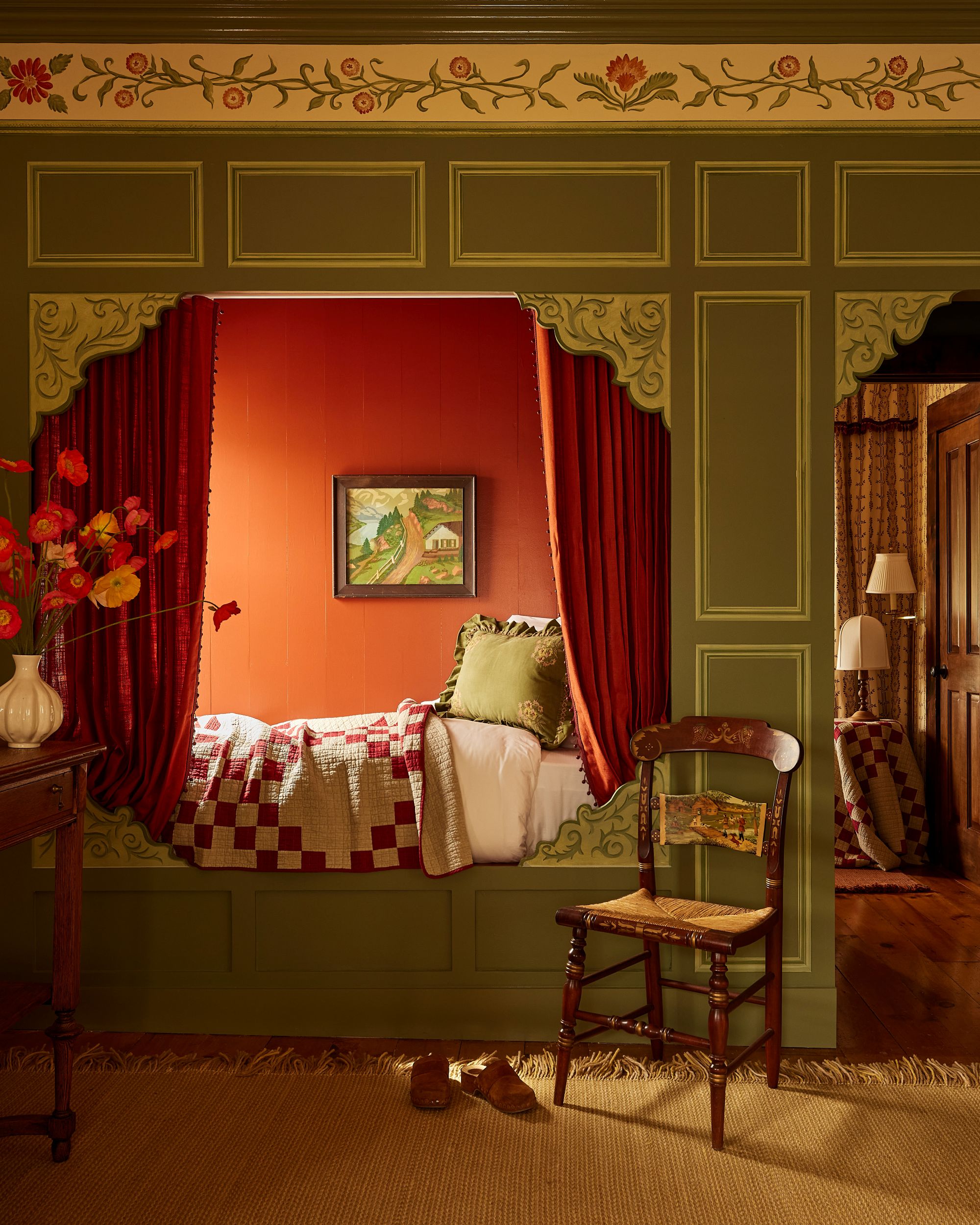 a built-in bed with a patchwork quilt, red curtains to hide the bed, and decorative wall detailing