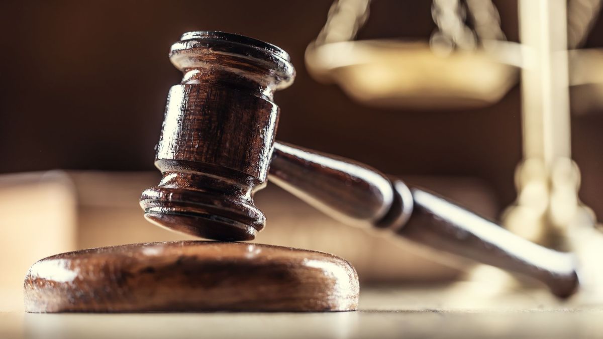 A wooden judges&#039; gavel in the foreground with a golden set of scales in the backgroundr