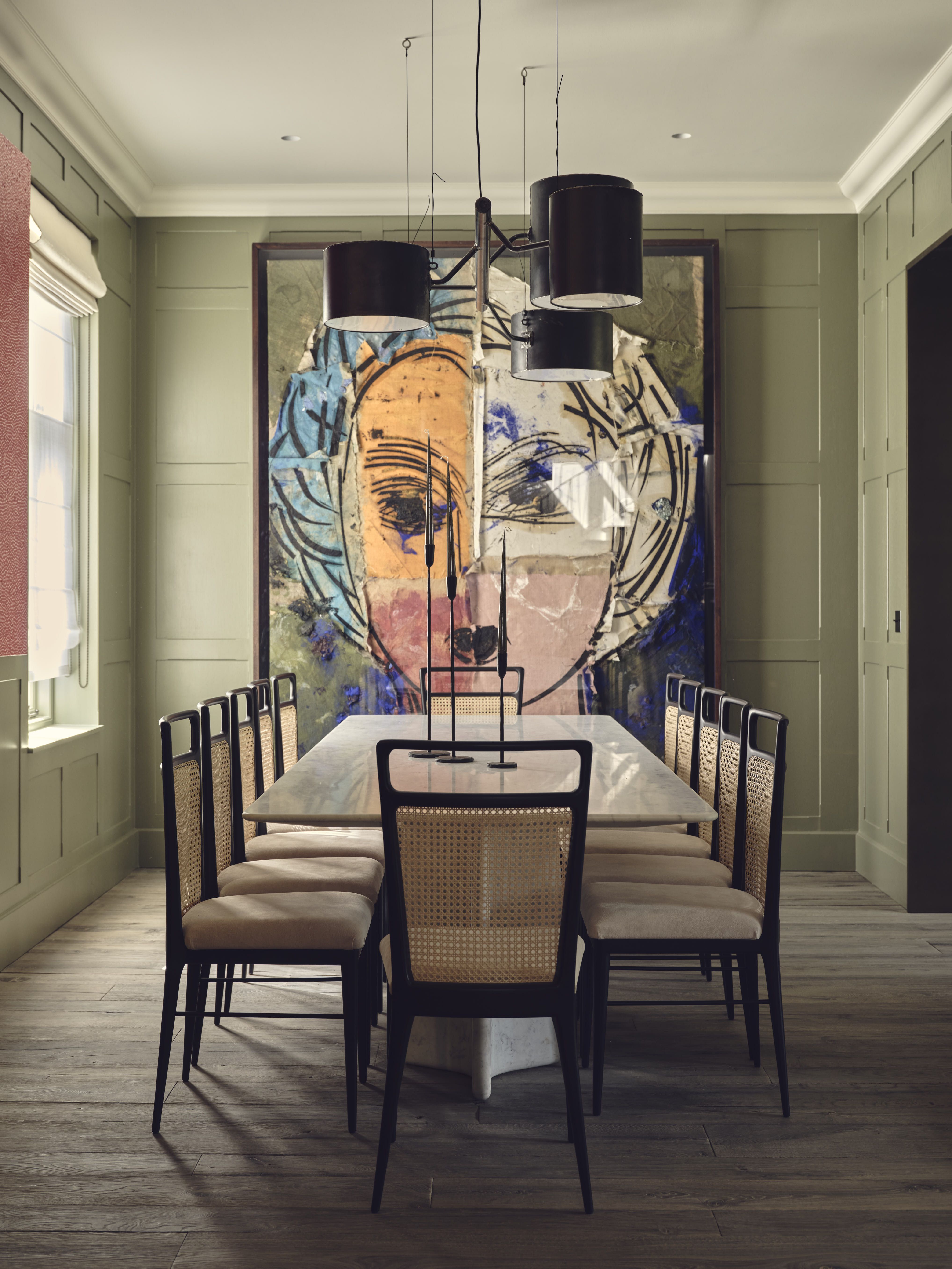 dining room with long table and cane chairs, large artwork with timber floors and green wall panelling and pendant lights