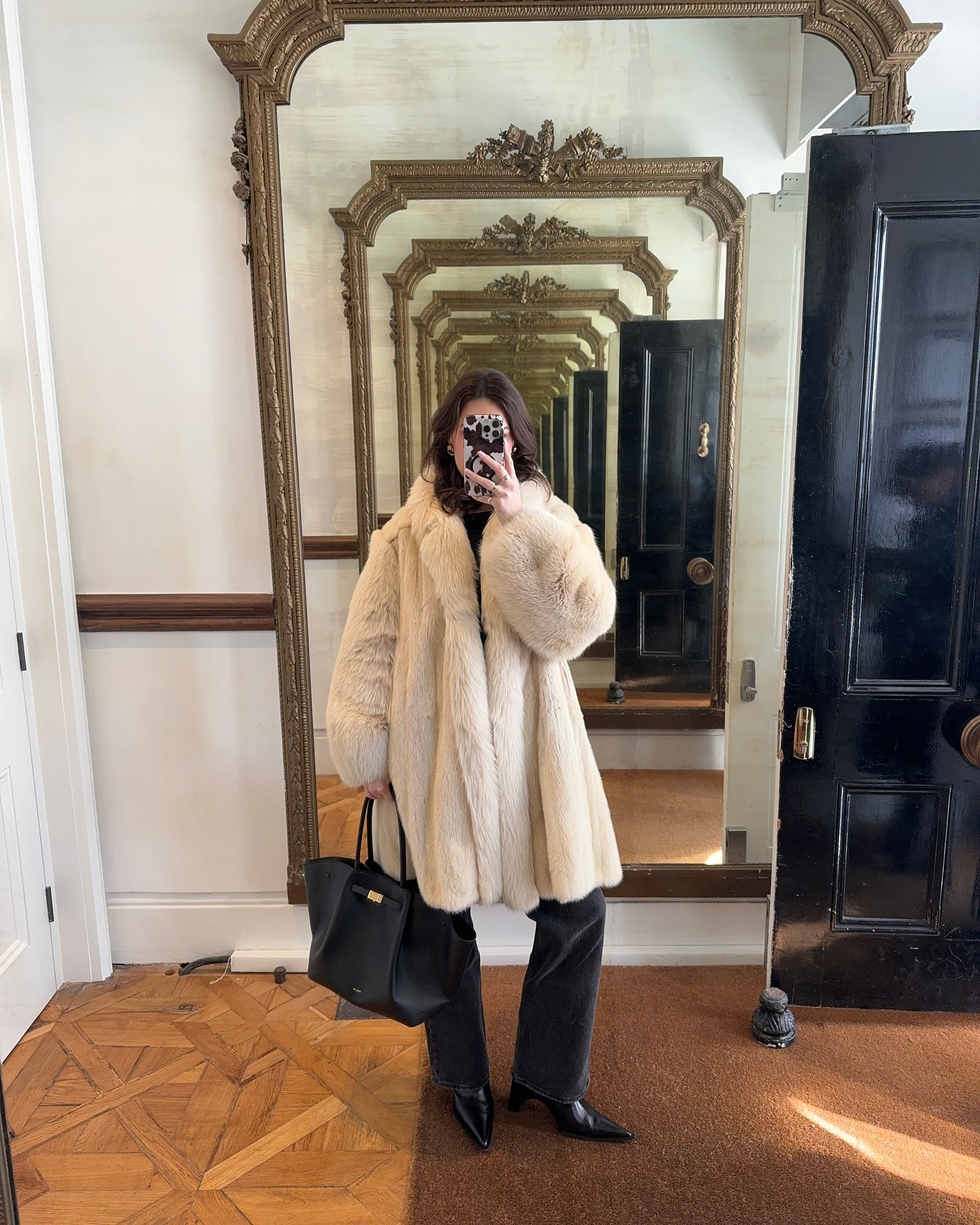 @maggie_mccormack wears a white fur coat, black jeans, pointed-toe boots, and a black tote.