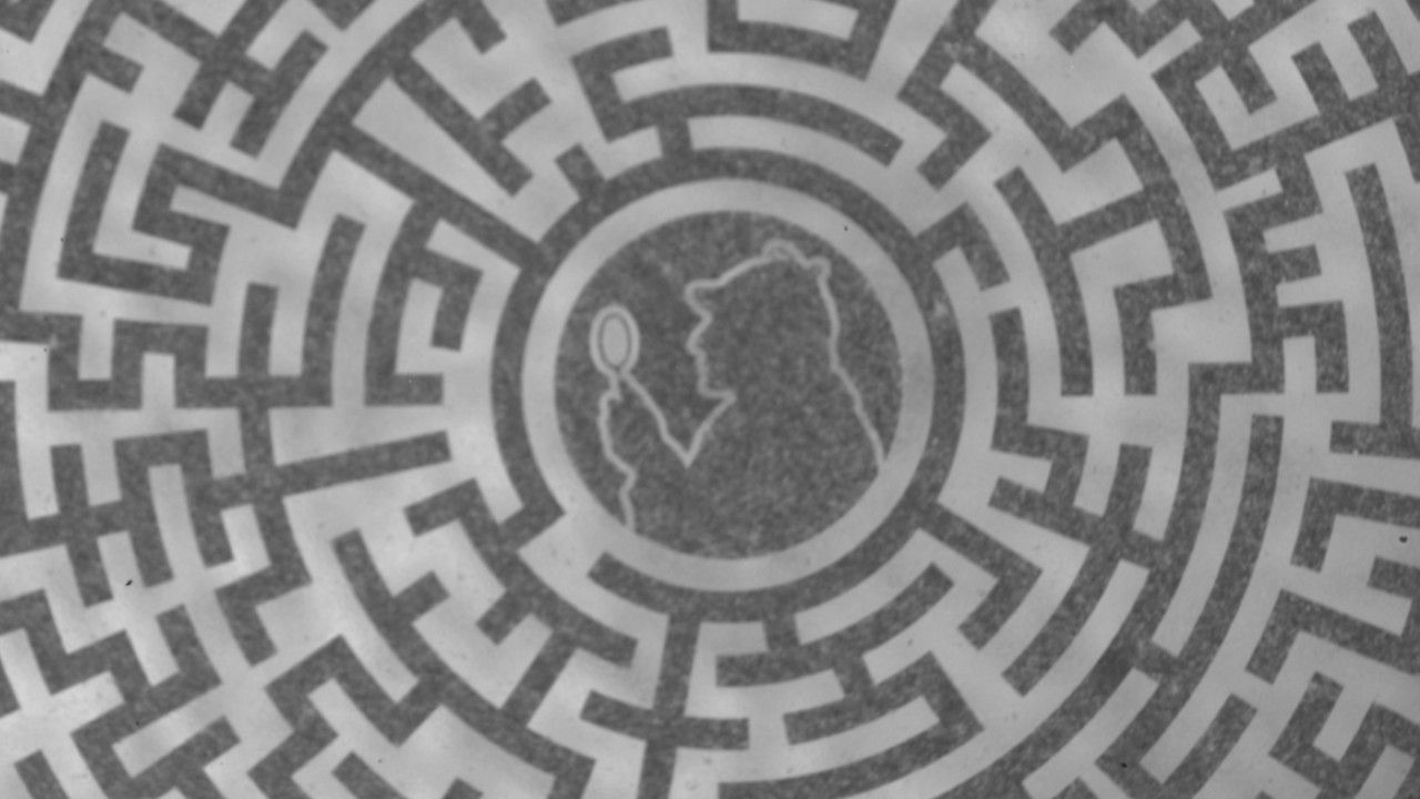 a silhouette of a man in a hat looking through a magnifying glass, in the center of a labyrinth etched onto metal