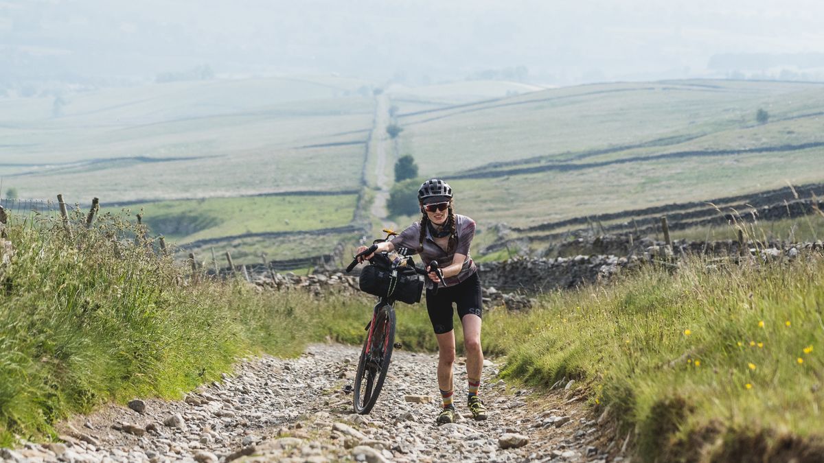 A cyclists pushes up a long gravel road