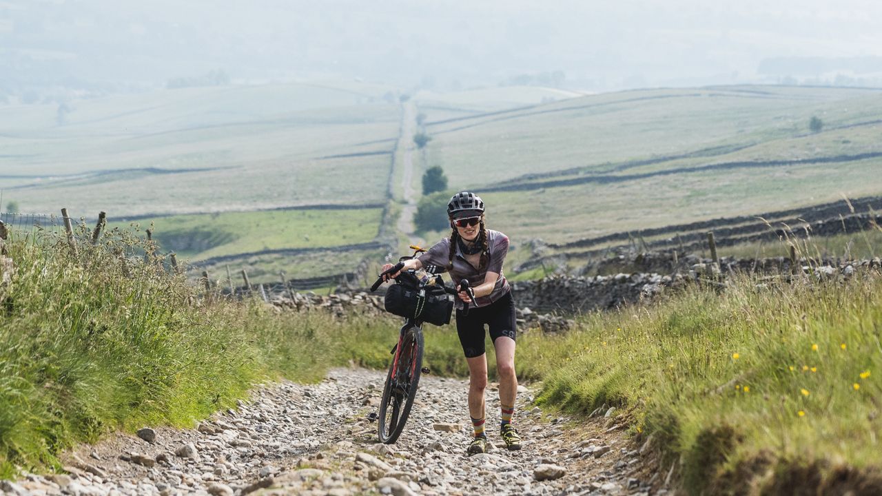 A cyclists pushes up a long gravel road