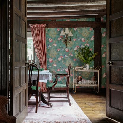 dining room in a medieval house with wall and ceiling beams. floral wallpaper and dark panelled doors