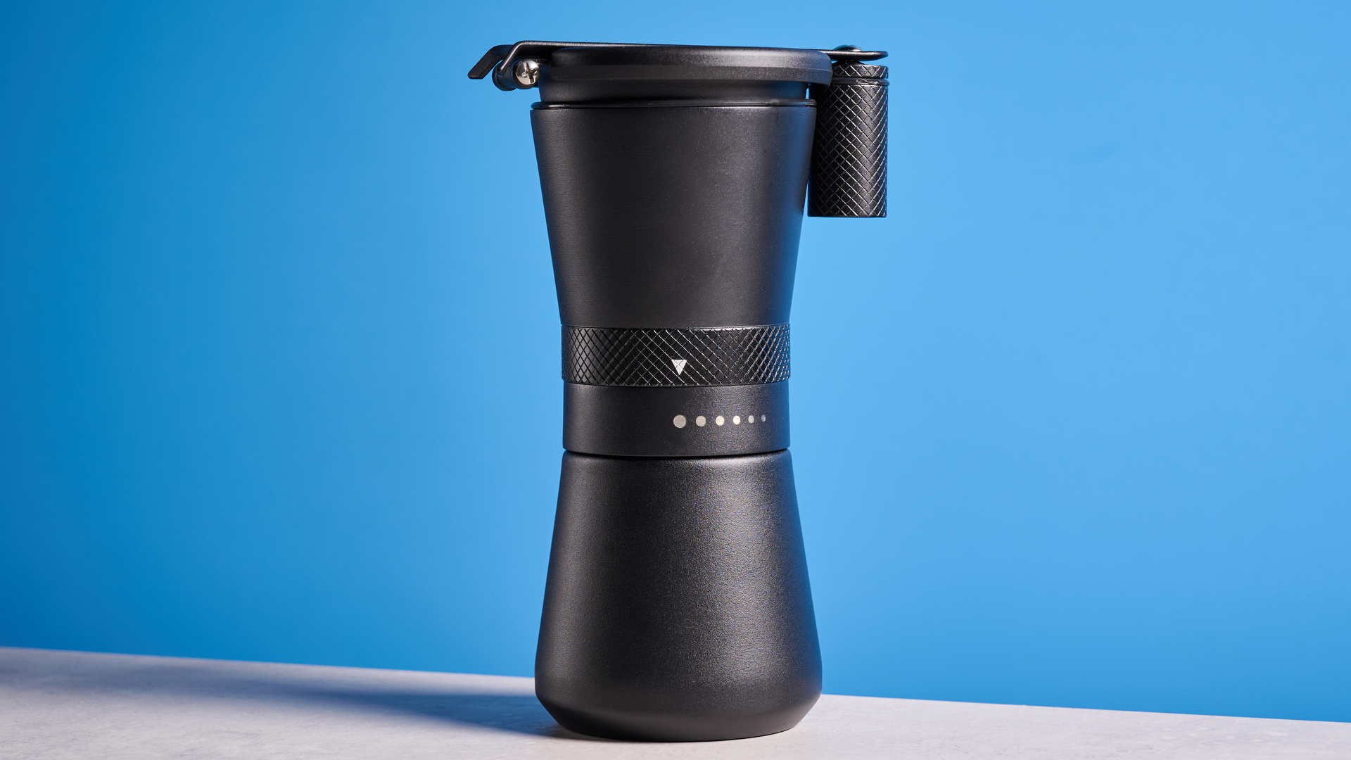 MiiR New Standard Hand Grinder in matte black photographed in front of a blue background