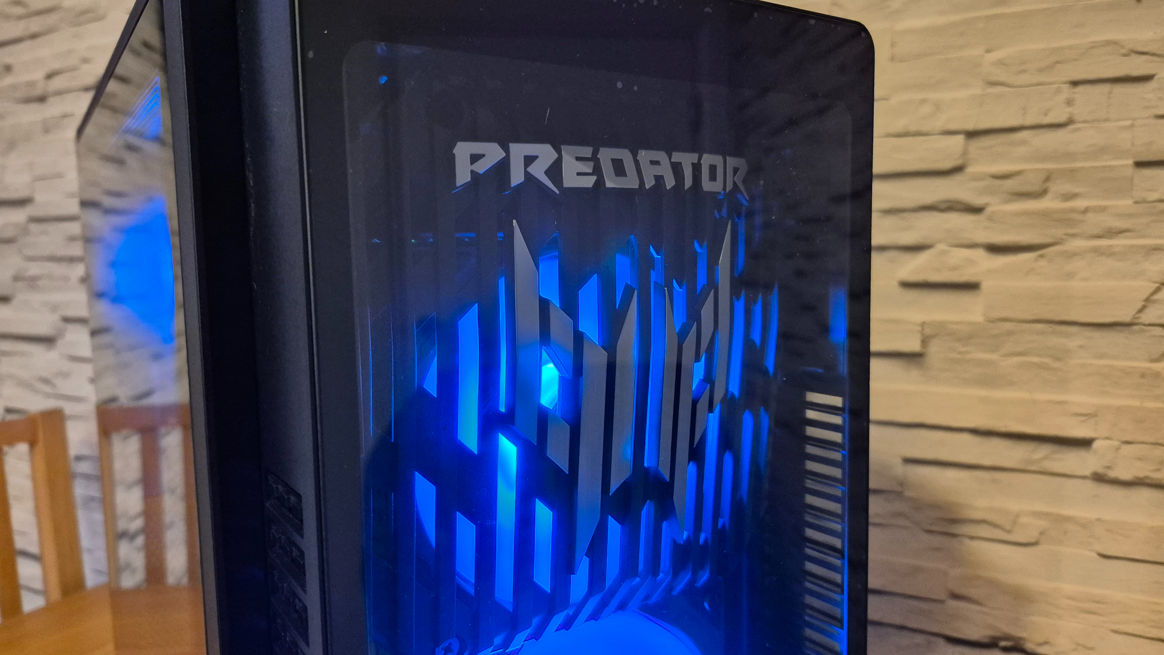 A close up of an Acer Predator Orion 5000 gaming PC sitting on top of a wooden surface infront of a white brick effect wall