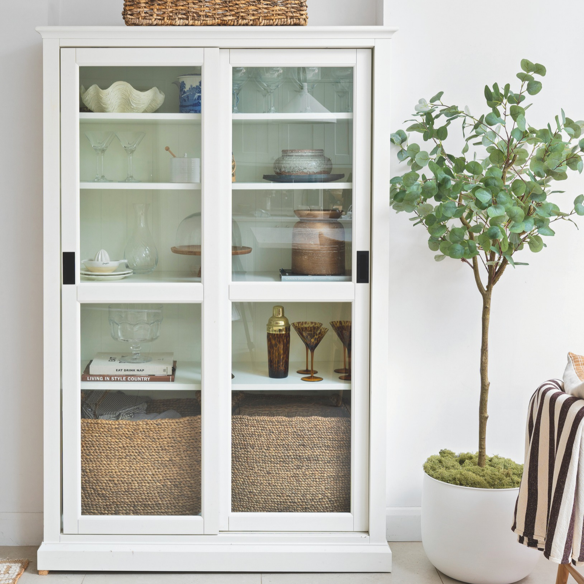 White wooden cabinet with glassware, bakeware and kitchen decor.