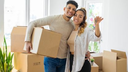 Happy young couple standing in front of moving boxes and holding up their new house keys