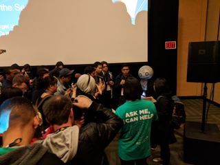 Yoko Taro wearing his usual mask, surrounded by fans after his talk.