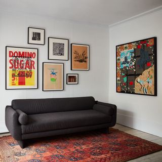 Many paintings of different sizes are hung on the wall, above a dark gray sofa.