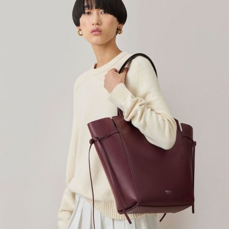 Woman wears cream jumper and burgundy tote bag