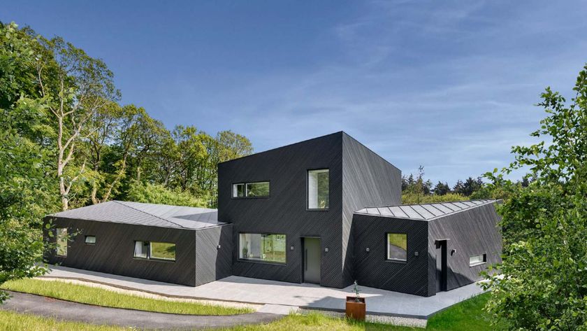 A contemporary black timber-clad home made up of three angular sections; the central section is two storeys, while the two sections either side are single storey. The house is surrounded by woodland.