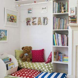 childrens bedroom with white wall and cabinet with books and cushions with teddy bear