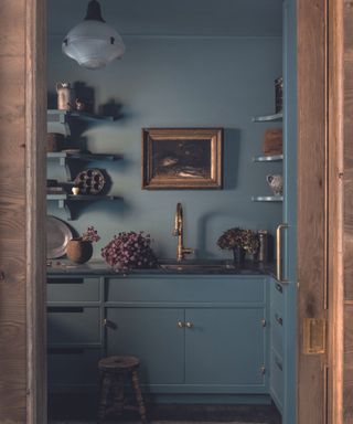 blue kitchen with brass fittings and art on walls and open shelves