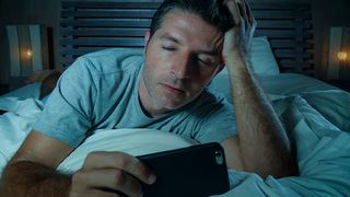 Tired man looking at his smartphone in bed