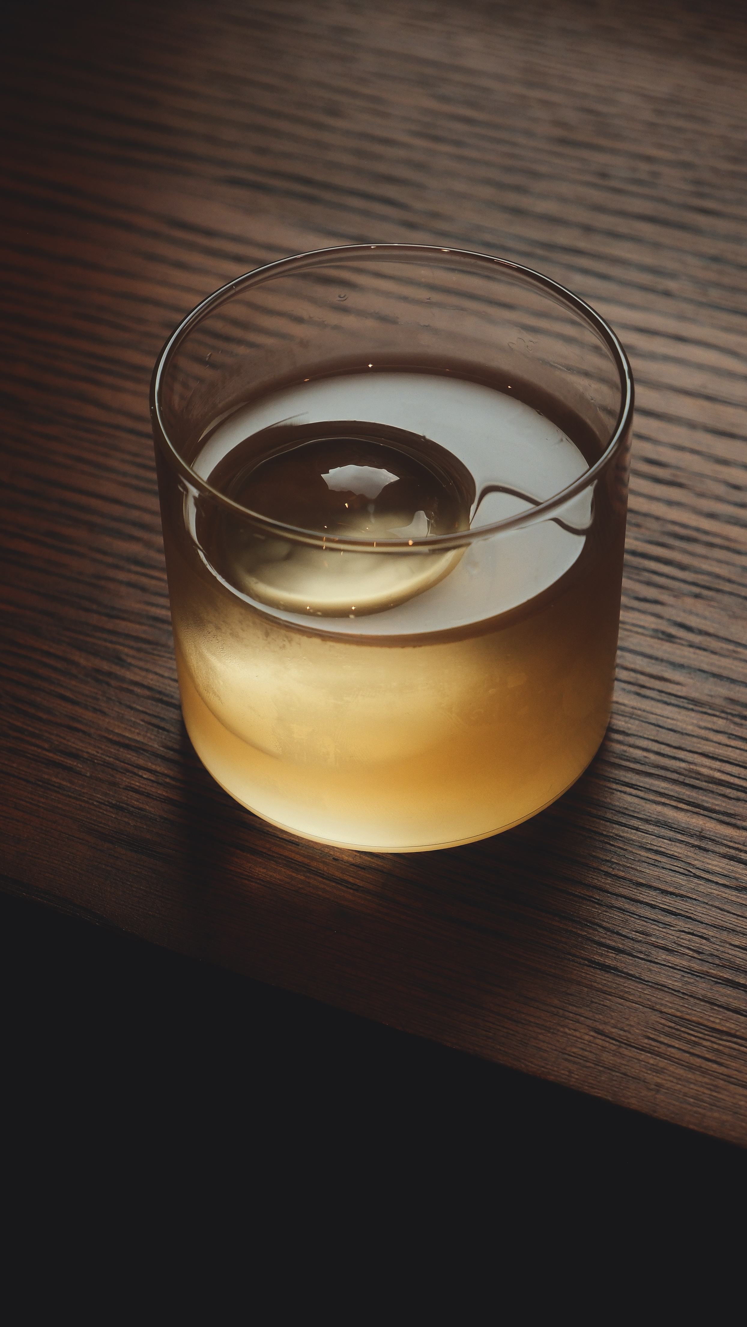 The Rhubarb and Loveage cocktail, a bronze semi-opaque cocktail served in a tumbler with a large ice cube