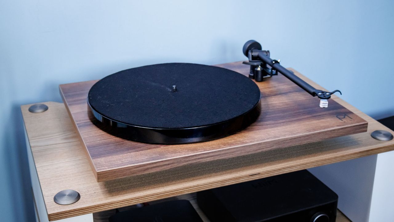 A wood finish Rega Planar 1 Plus turntable in front of a blue wall