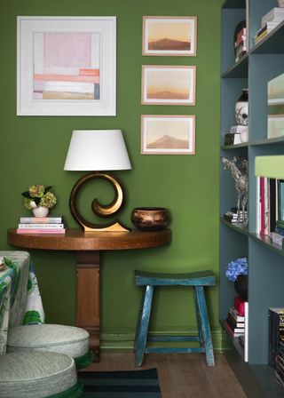 green wall with art, table and lamp in front