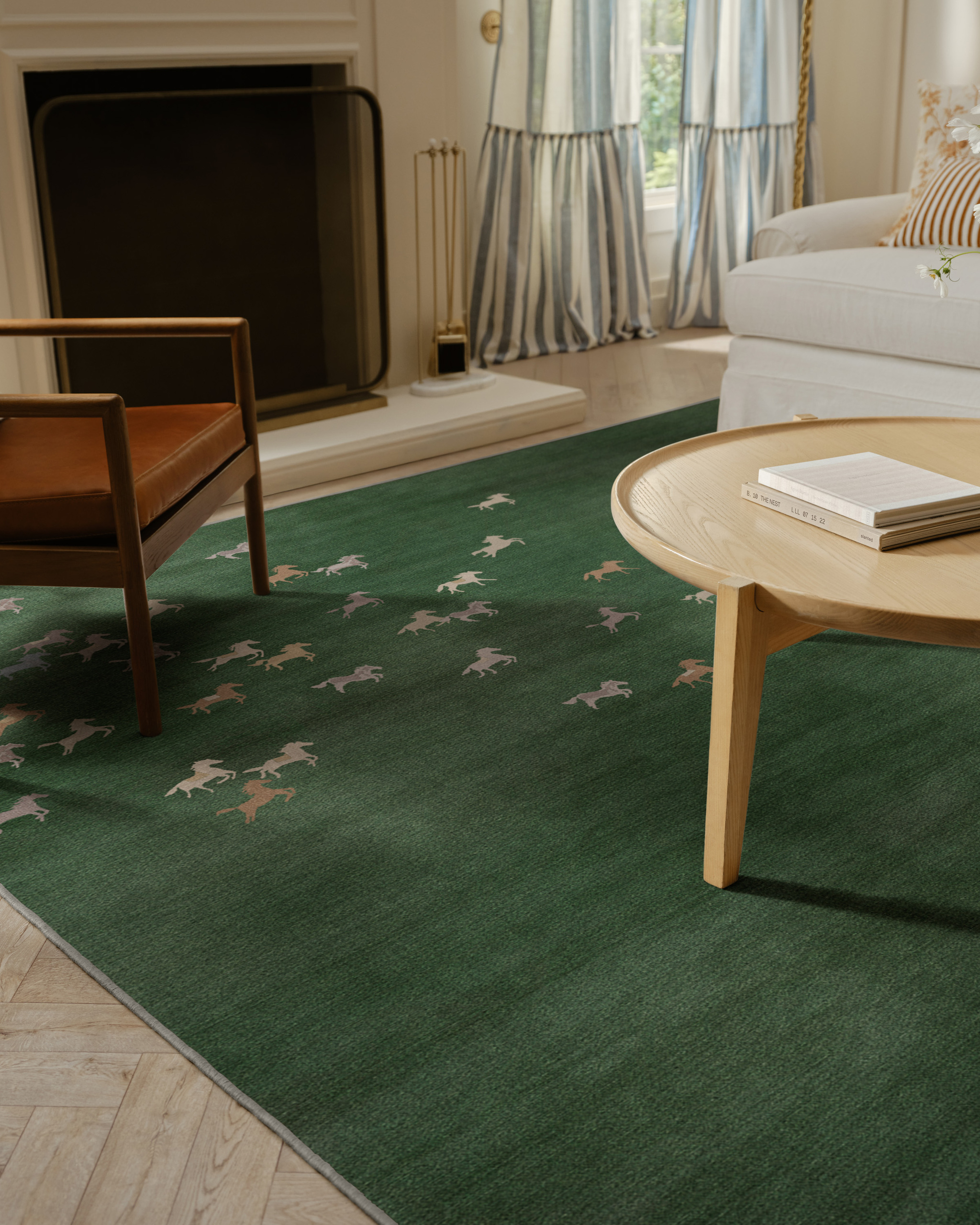 Image of a dark green rug with multi-colored horses on it in a living room with a round wooden coffee table, a white sofa, a fireplace, and a brown leather accent chair.