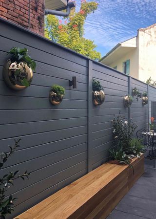 Backyard ideas on a budget incorporating privacy in the form of a black painted fence with wall mounted planters and bench seating in an urban yard.